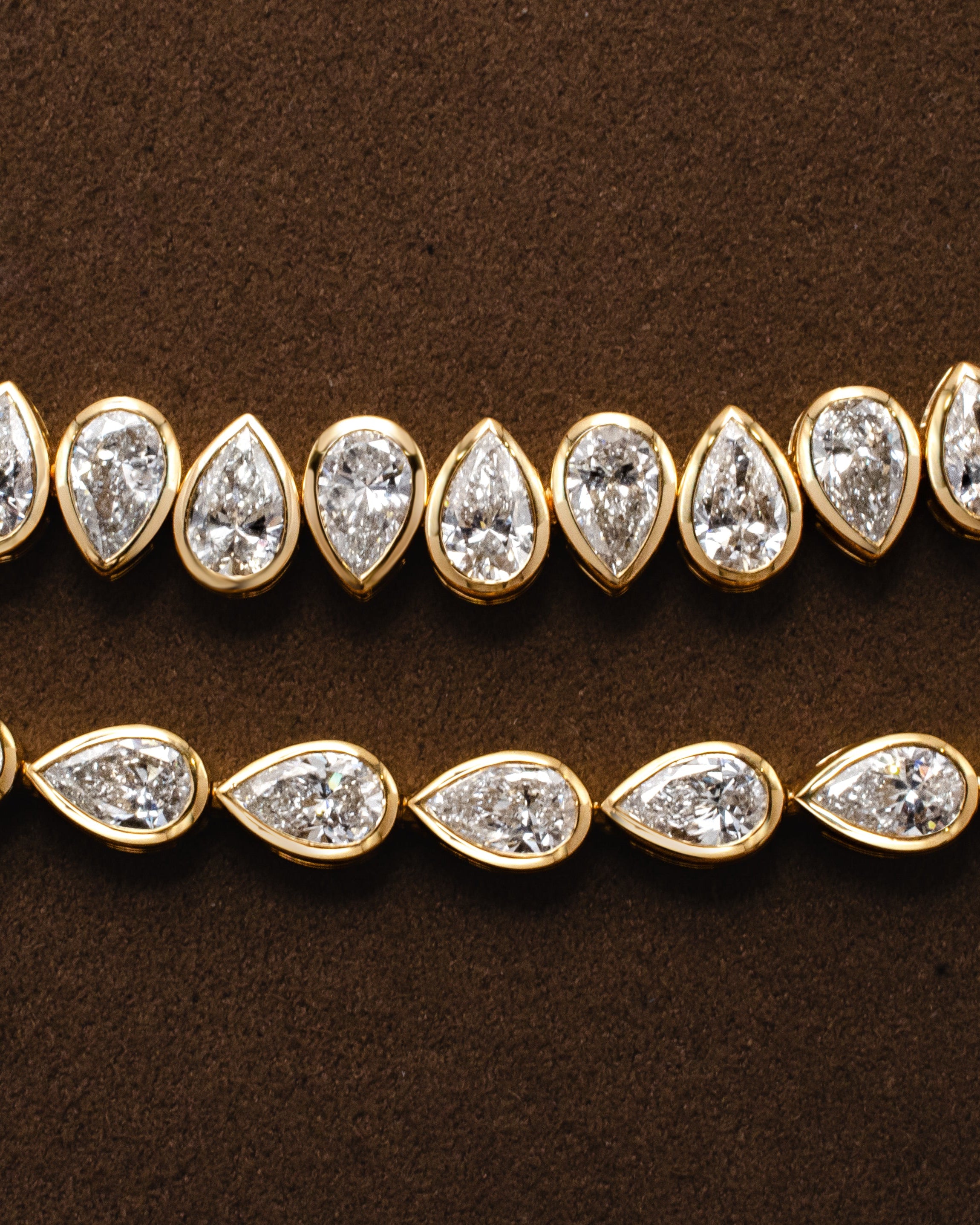 two gold tennis bracelets with bezel set pear shaped diamonds 
