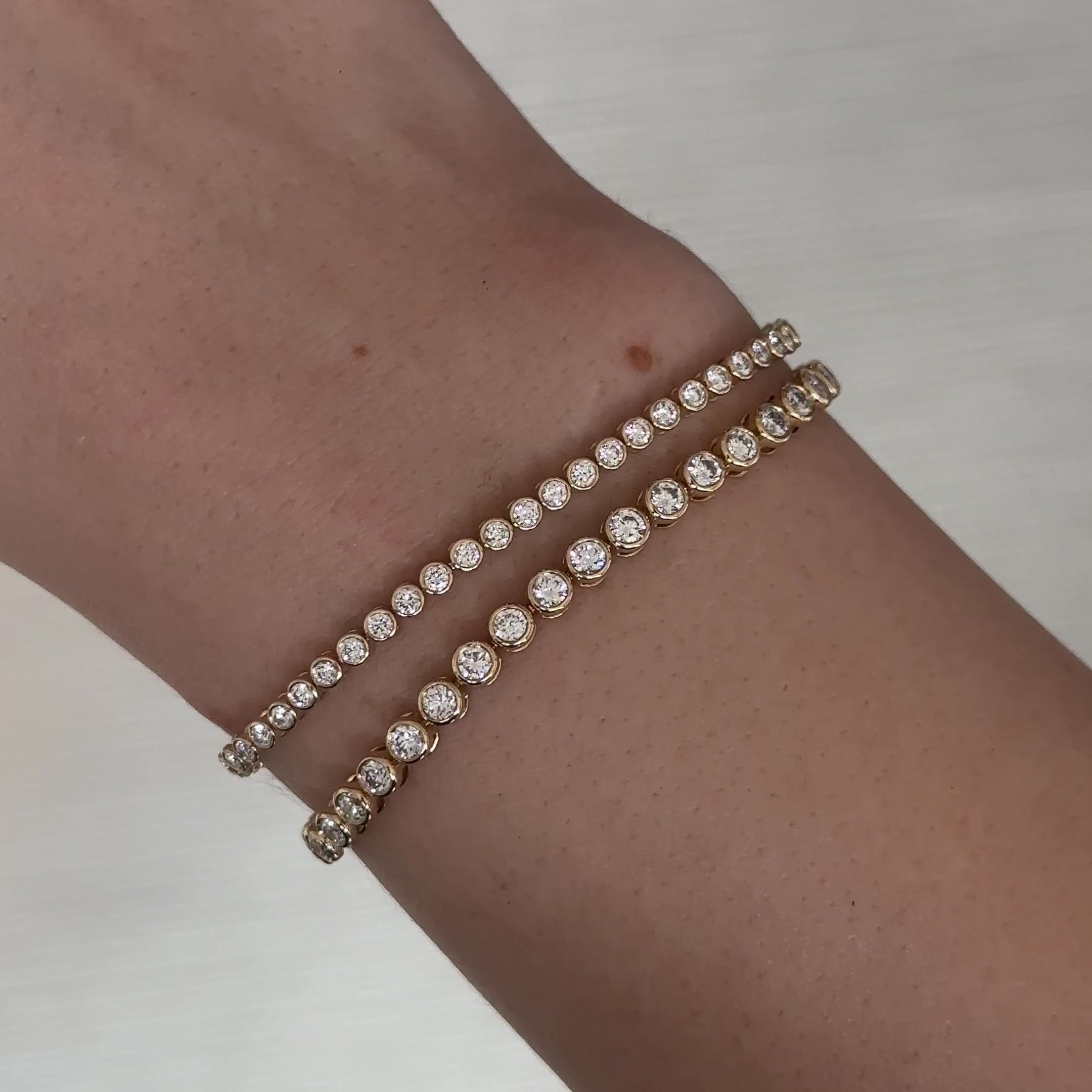 Close up of a wrist with two gold tennis bracelets with bezel set diamonds